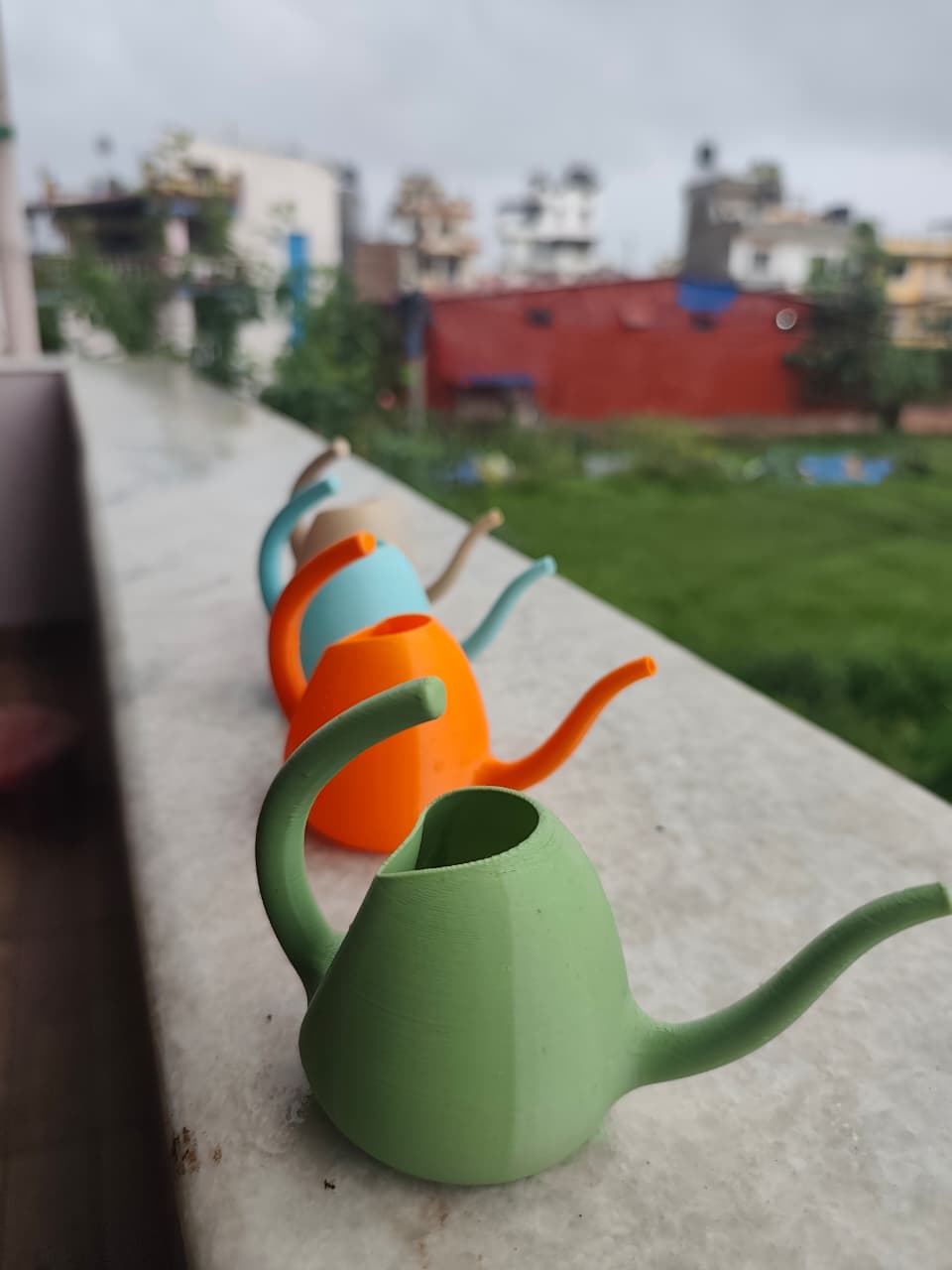 A lineup of Tippy watering cans in green, orange, turquoise, and beige
